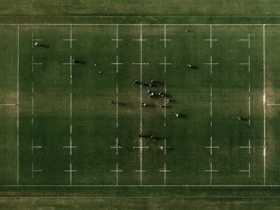 Vue aérienne stylisée d’un terrain de rugby avec lignes de craie et plots marquant les positions