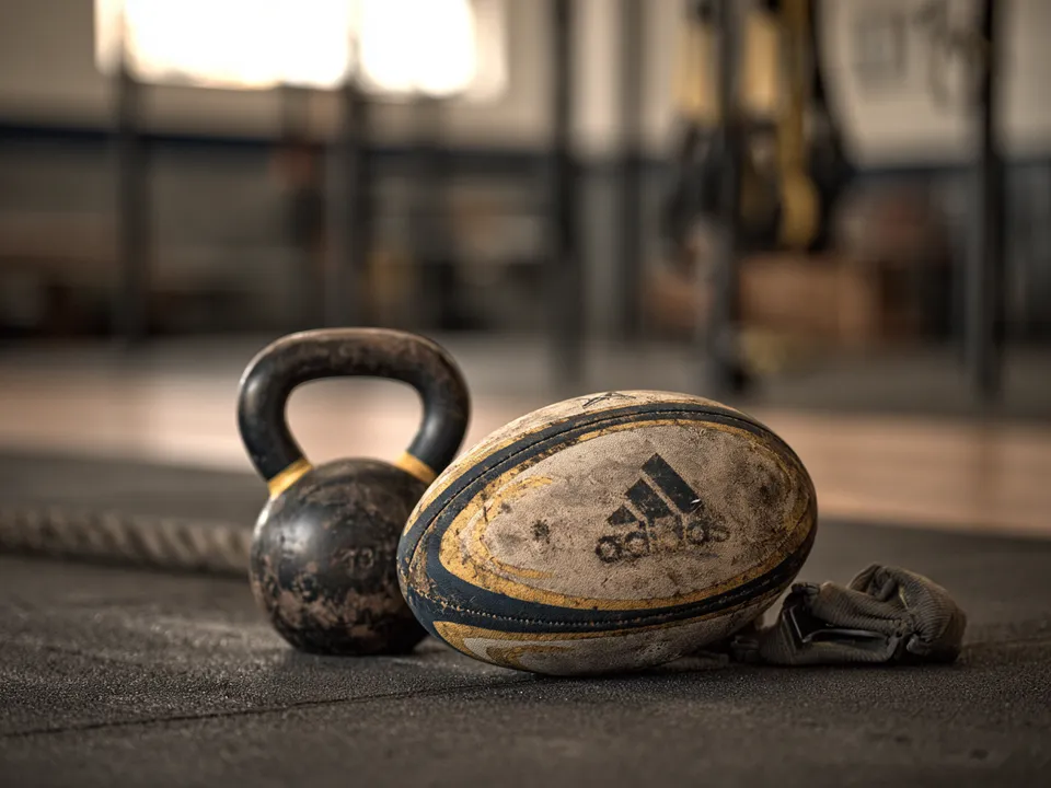 Ballon ovale posé au sol à côté d’une kettlebell et d’une bande élastique dans une salle de musculation